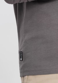 Graues Langarmshirt mit glatter Oberfläche. Verfügt über ein schwarzes Etikett mit der Aufschrift "ombre" am Saum. Einfaches Design, keine Muster oder Akzente.