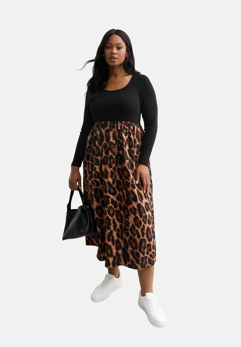 Maglietta nera a maniche lunghe abbinata a una gonna con stampa leopardata, dotata di vita elastica. Indossata con sneakers bianche e una borsa nera.