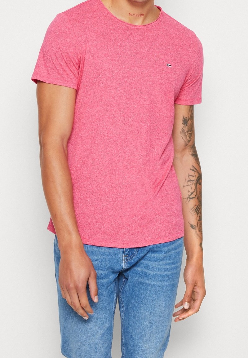 Red short-sleeve t-shirt made of soft fabric with a crew neck. Features a small logo on the chest and a relaxed fit. Worn with blue denim jeans.