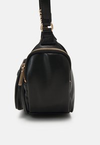 Bolso de mano de piel negra con forma estructurada, cremalleras en tono dorado y una correa desmontable. Presenta una textura suave y sutilezas en los detalles de costura.