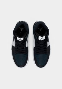 Tumedrohelised ja mustad tossud, millel on perforatsioonidega varbaosa, mustad paelad, valged tallad ja Jordan'i logo keelel ning pahkluu piirkonnas.