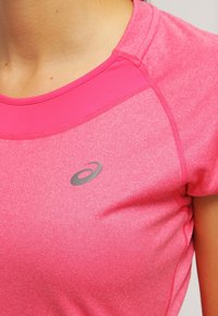 Pink athletic shirt made of textured fabric, featuring short sleeves, a round neck, and a gray logo on the front.