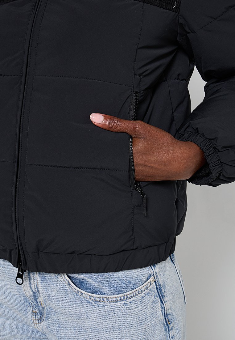 Schwarze Steppjacke mit einem gesteppten Design, Reißverschlusstaschen und elastischen Bündchen. Das Material hat eine glatte, matte Oberfläche.
