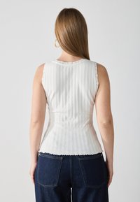 White ribbed tank top with scalloped edges; fitted design highlights the waist, featuring lace accents on shoulders and neckline.