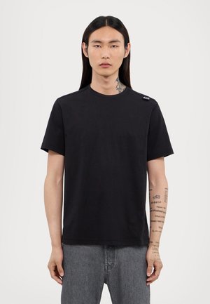 Camiseta corta de manga negra hecha de una tela suave, con un escote redondo y una pequeña etiqueta de marca en el hombro.