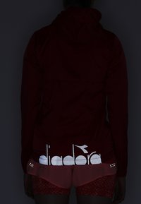 Red hooded jacket with reflective logo detailing at the back, paired with light pink shorts featuring a textured pattern and additional accents.