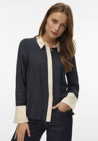 Camisa de manga larga azul marino con cuello y puños crema claro, con tapeta abotonada y acabado texturizado. Ajuste casual y diseño moderno.