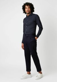 Marineblaues Langarmhemd mit kleinem Punktmuster, kombiniert mit maßgeschneiderten dunklen Hosen und weißen Sneakers, die einen smart-casual Look kreieren.