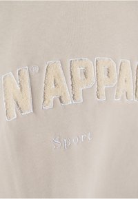 Bežová mikina s texturovanou krémovou výšivkou slova "N'APPA" a slova "Sport" v bílé barvě. Hladká bavlněná tkanina.