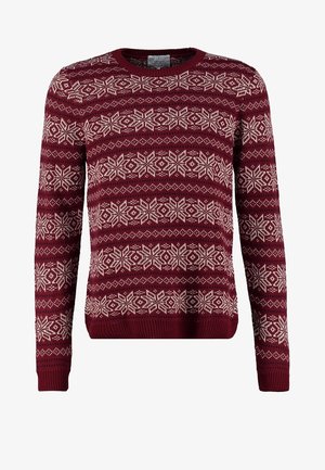 Cappotto pea in lana grigio con bottoni doppiopetto, indossato su un maglione bordeaux con motivo. Jeans skinny neri e stivaletti completano l'outfit.