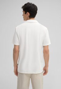 Witte polo met korte mouwen, van een textuurstof met een subtiel patroon, klassieke kraag en rechte zoom, gedragen met lichtbeige textuurbroek.