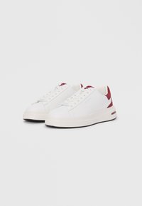White sneakers with a smooth leather upper and textured red heel accents. Features flat laces and a thick white rubber sole with black trim.