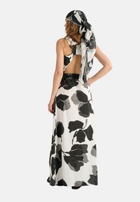 Abito maxi in tessuto bianco con grandi motivi floreali neri e grigi. Presenta una schiena scoperta, abbinato a una sciarpa coordinata. Sandali flat.