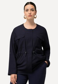Granatowa kurtka z dwiema kieszeniami na piersi, �ściągnięta w talii, z detalami ze sznurkiem. Gładki materiał, luźny krój i długie rękawy.