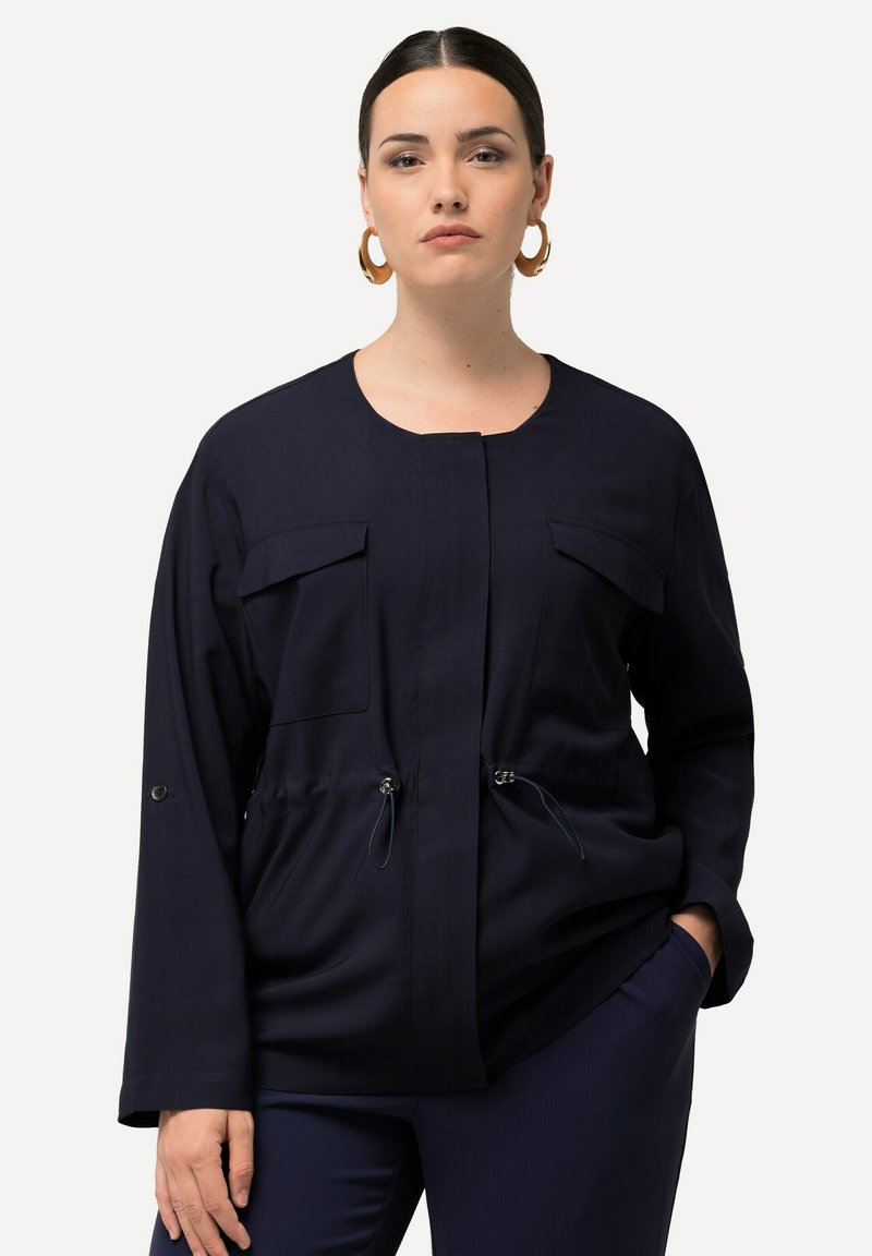 Granatowa kurtka z dwiema kieszeniami na piersi, ściągnięta w talii, z detalami ze sznurkiem. Gładki materiał, luźny krój i długie rękawy.