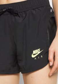 Černé sportovní šortky s elastickým pasem, šňůrkou a síťovinovými bočními panely. Obsahují neonově žluté logo Nike a text "AIR".