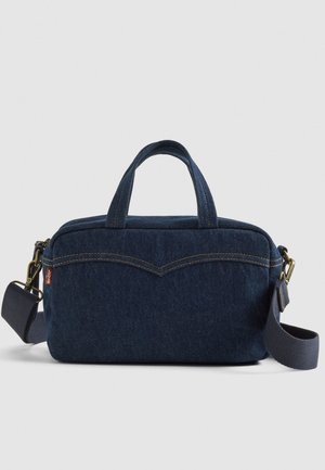 Bolso rectangular de mezclilla azul oscuro con asas cortas, correa de hombro desmontable y detalle de costuras amarillas en la parte frontal.