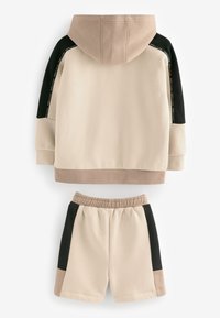 Beige og sort todelt sæt med en hættetrøje med kontrasterende ærmer og matchende shorts med farveblokke på siderne.