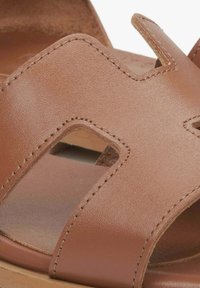 Bruine leren sandaal met een uitsnijdingen ontwerp, gladde textuur en gestikte details. Open teen met een zachte zool voor comfort.