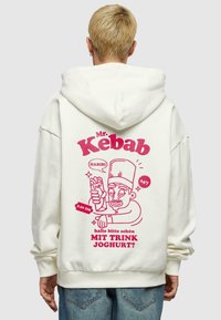 Kremfarget hettegenser med et stort rosa grafikk på baksiden, som viser en karakter som holder en kebab, med tekst og dekorative elementer.