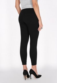 Fekete, magas derekú skinny farmernadrág sima felülettel és szoros szabással. Két hátsó zsebbel és elegáns kialakítással rendelkezik, fekete magassarkú cipővel párosítva.