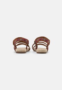 Sandali marroni con cinturini intrecciati colorati, suole in stile espadrille texturizzate e fibbie regolabili. Tacco piatto per il comfort.