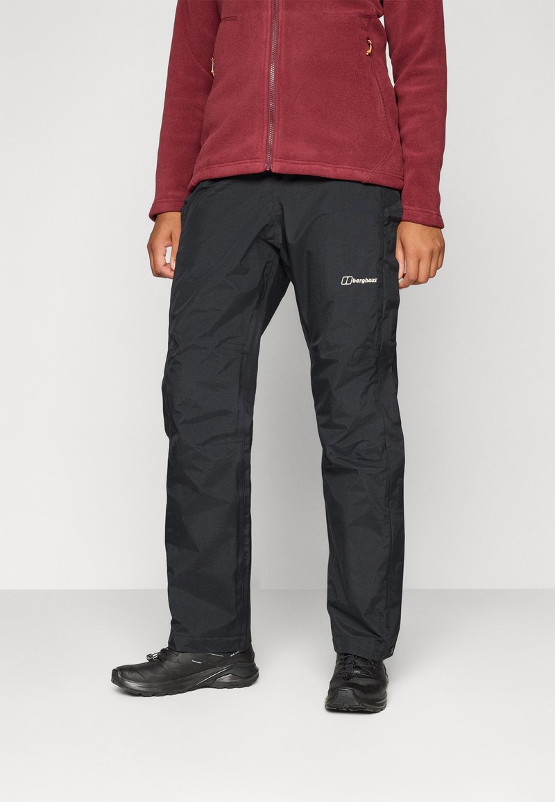 Model nosi bordo zip-velur i crne vodonepropusne hlače s logom, stojeći ispred jednostavne svijetle pozadine.