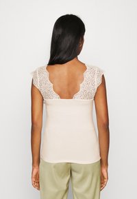 Beżowa bluzka z koronkowym tyłem i krótkimi rękawami, z głębokim dekoltem w kształcie V. Gładki materiał typu jersey o dopasowanym kroju.