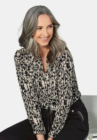 Zwarte en crèmekleurige blouse met een V-hals, lange mouwen en gathered cuffs; gecombineerd met zwarte broek met koord.