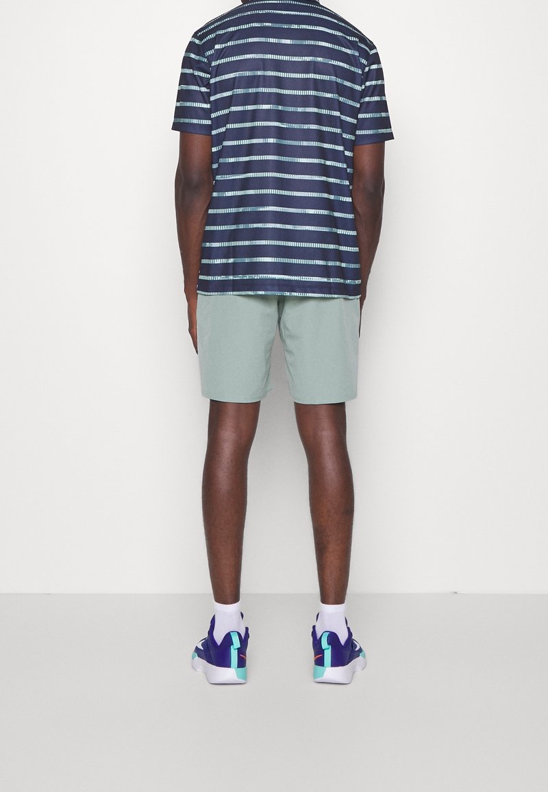 Une chemise à rayures marines à manches courtes, un short vert clair et des baskets violettes avec des accents en teal. Présente une coupe décontractée et un design casual.