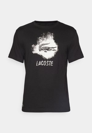 Camiseta de algodón negra con un gráfico de cocodrilo blanco y la palabra "LACOSTE" debajo, cuello redondo, mangas cortas y corte estándar.