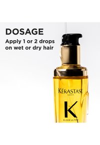 Kérastase Elixir Ultime haarolie in een transparante, amberkleurige fles met een zwarte pomp, gouden accenten en een zichtbare druppel olie.