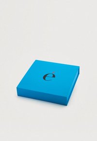 Μπλε χαρτόκουτο με ομαλή υφή, που διαθέτει ένα μαύρο λογότυπο με κόκκινη λεπτομέρεια στην κορυφή. Το κουτί έχει κομψή, ορθογώνια μορφή.