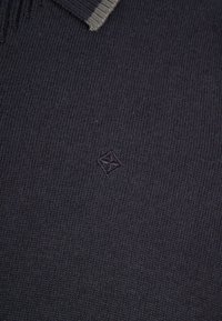 Ciemnoszary dziergany sweter z prążkowanym kołnierzem, z subtelnym wytłoczonym logo na klatce piersiowej. Miękka faktura i równe szwy.