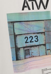 Verbleekt blauw industrieel gebouw met groot zwart nummer "223" boven een gesloten metalen deur, zachte pastelkleurige grond ervoor.