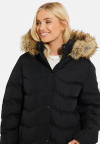 Zwarte pufferjack met een afneembare nepbontkap, knopen aan de voorkant en een gewatteerde textuur, ontworpen voor warmte en comfort.
