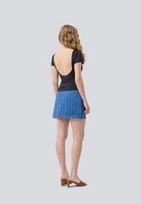 Black short-sleeve top with a deep back cut, paired with a blue denim mini skirt featuring vertical white stripes. Worn with brown heeled sandals.