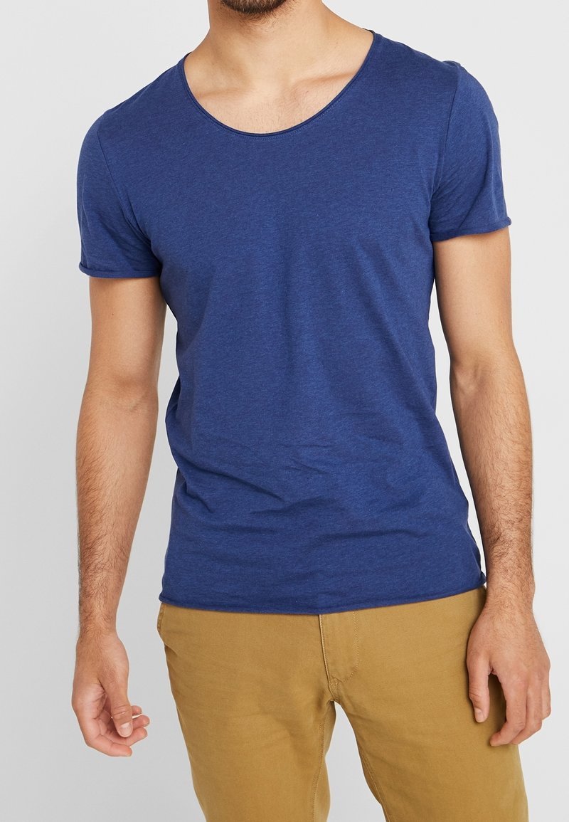 Blå kortärmad t-shirt med rundad halsringning, tillverkad av mjukt tyg, något åtsittande med synliga sömmar, tillsammans med khakifärgade byxor.