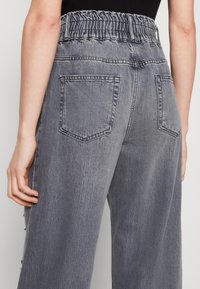 Pantalones de mezclilla gris con cinturilla elástica, dos bolsillos traseros y un diseño relajado de pierna ancha con una textura sutil.