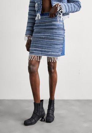 Blauer gewebter Rock mit fransigen Kanten und seitlicher Schlitze, kombiniert mit schwarzen Ankle Boots mit einzigartigen geschwungenen Absätzen und Reißverschluss.