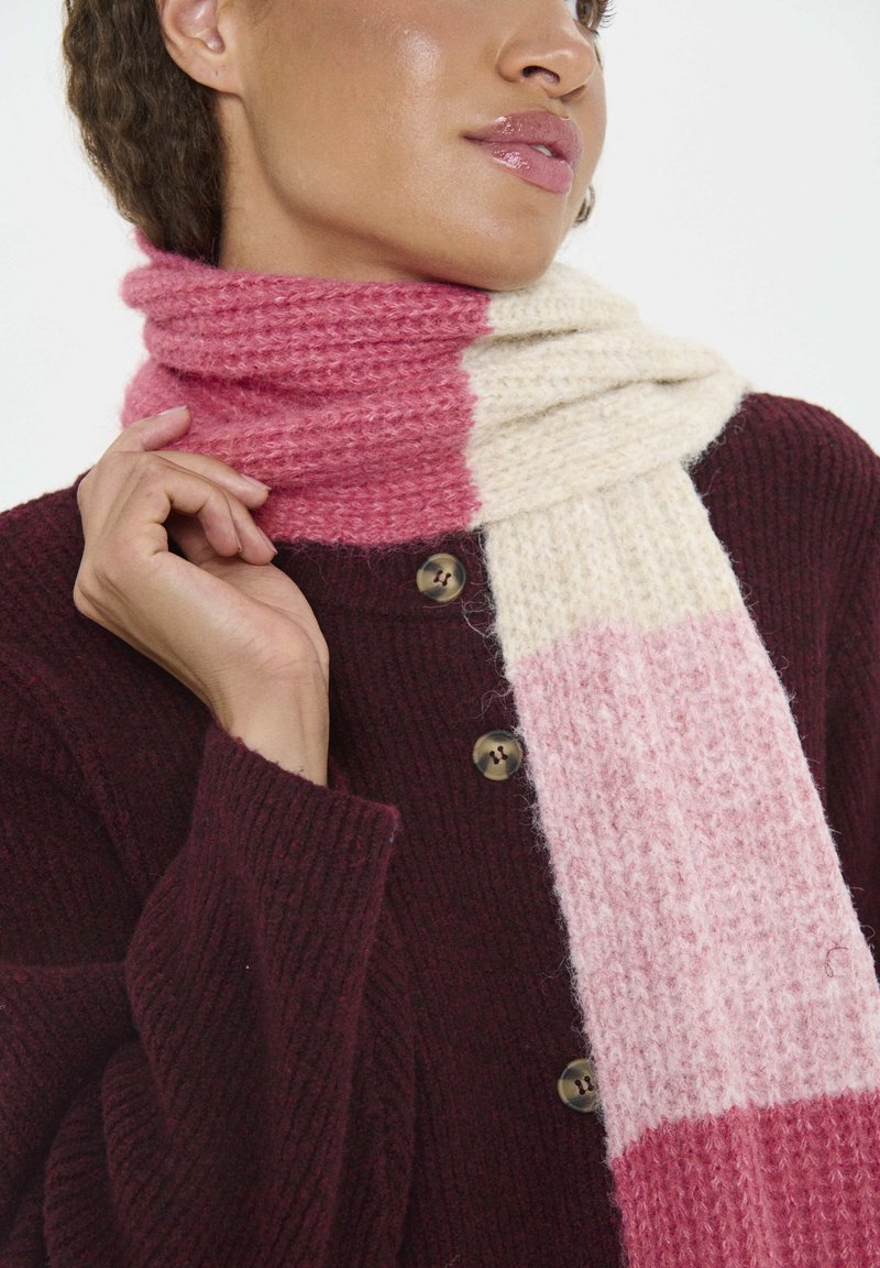 Strikket tørklæde med et gradientdesign i pink og cremefarver, bundet omkring halsen, lavet af blødt uldmateriale med en tekstureret finish.