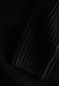 Black knit fabric featuring a textured pattern with prominent ribbed accents. The material appears soft and warm, suitable for colder weather.