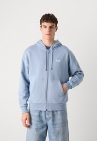 Lichtblauwe rits-houthoodie van een katoenmix met een voorzak, ribgebreide manchetten en een klein logopatch op de linkerborst.