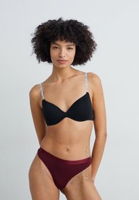 Black bra with adjustable straps and a tag, paired with maroon high-waisted panties. Smooth fabric texture, simple design, and minimal detailing.