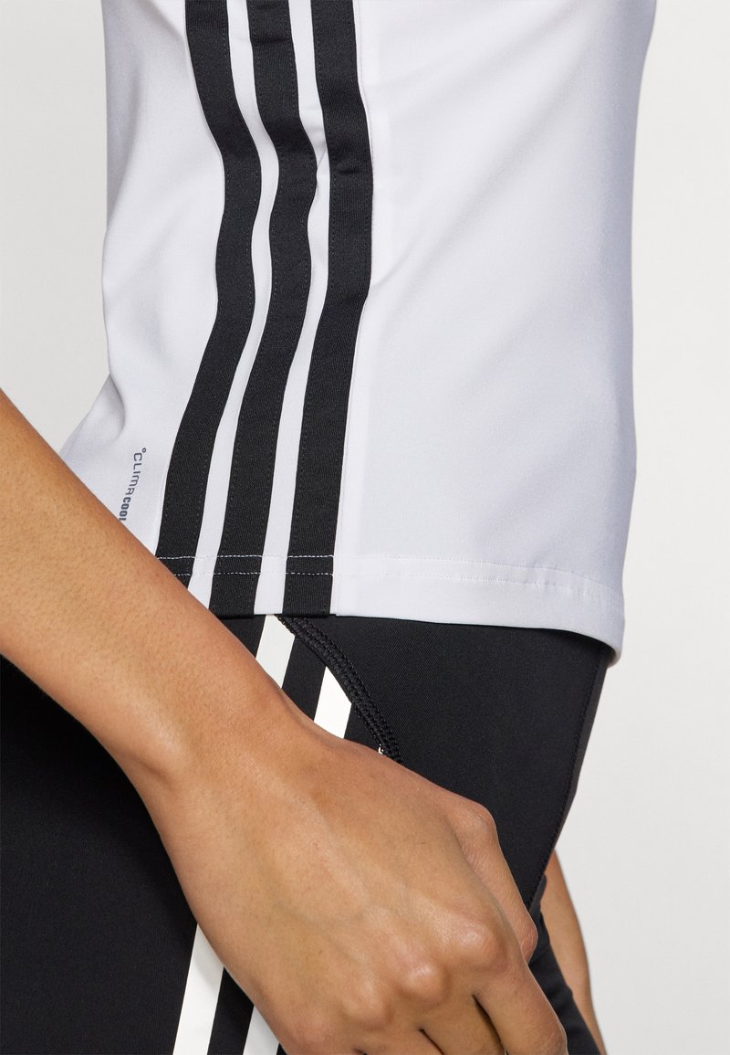 Maglietta sportiva a maniche corte di colore grigio chiaro con tre righe verticali nere, abbinata a pantaloni corti neri con accenti e cuciture bianche sui lati.