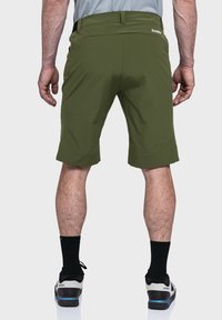 Grüne Shorts mit flachem Bund, elastischem Taillenbund und Seitentaschen; getragen mit schwarzen Socken und mehrfarbigen Schuhen. Minimales Design, glatte Textur.