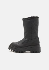 Botas de tobillo negras hechas de cuero texturizado con un dobladillo forrado de piel, suela de plataforma gruesa con bordes dentados y un sutil detalle de logo.