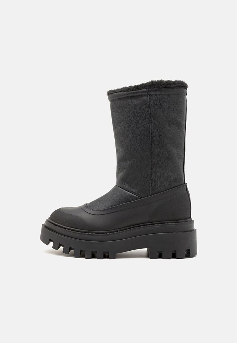 Botas de tobillo negras hechas de cuero texturizado con un dobladillo forrado de piel, suela de plataforma gruesa con bordes dentados y un sutil detalle de logo.