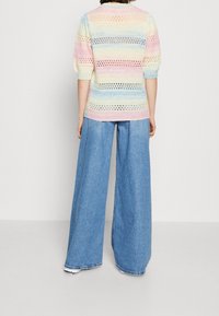Lekki, wielokolorowy sweter dzianinowy z pastelowymi paskami i ażurowymi detalami, w połączeniu z szerokimi niebieskimi dżinsami.