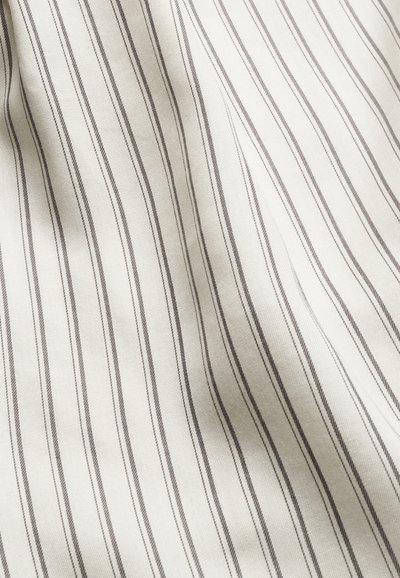 Fehér anyag vékony, függőleges fekete és szürke csíkokkal, lágy redőket és textúrát mutatva.